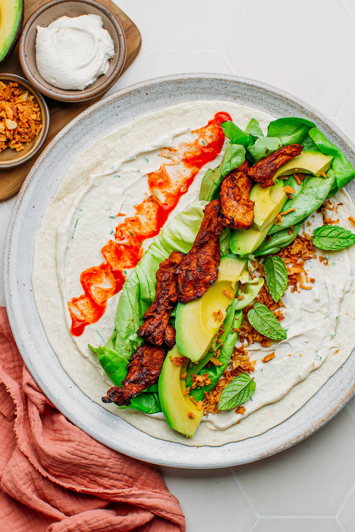 Flour tortilla topped with cream cheese, lettuce, avocado, and vegan chicken.