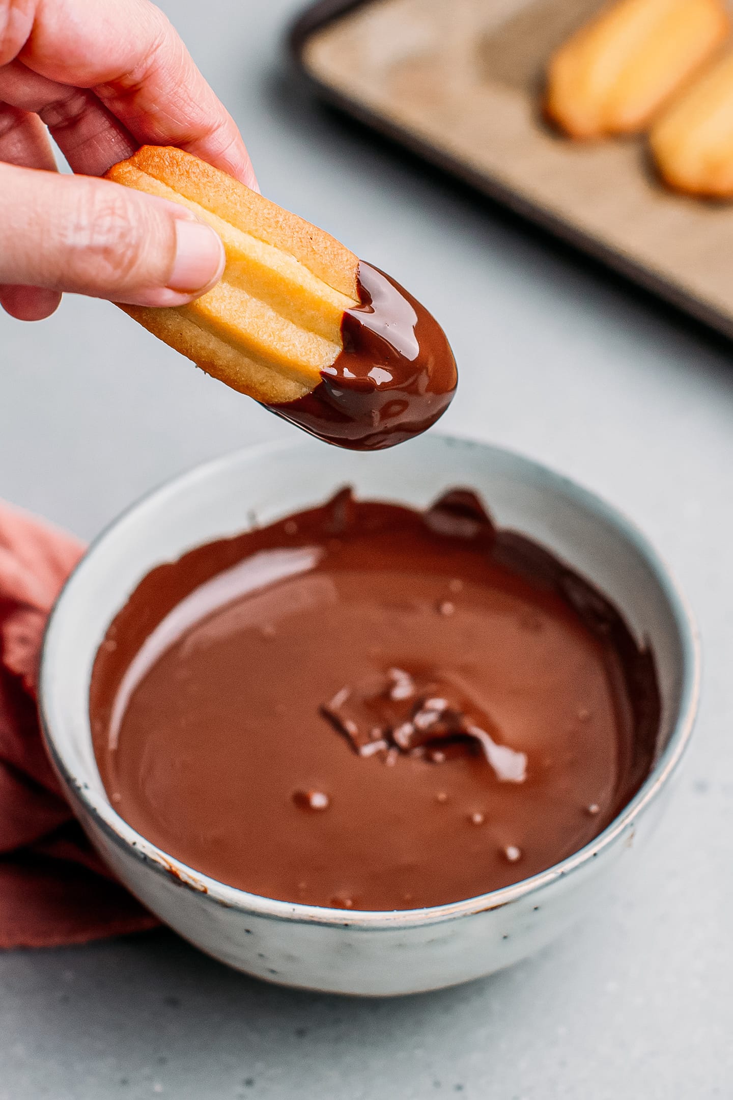 Dipping a vegan spritz cookie in melted dark chocolate.