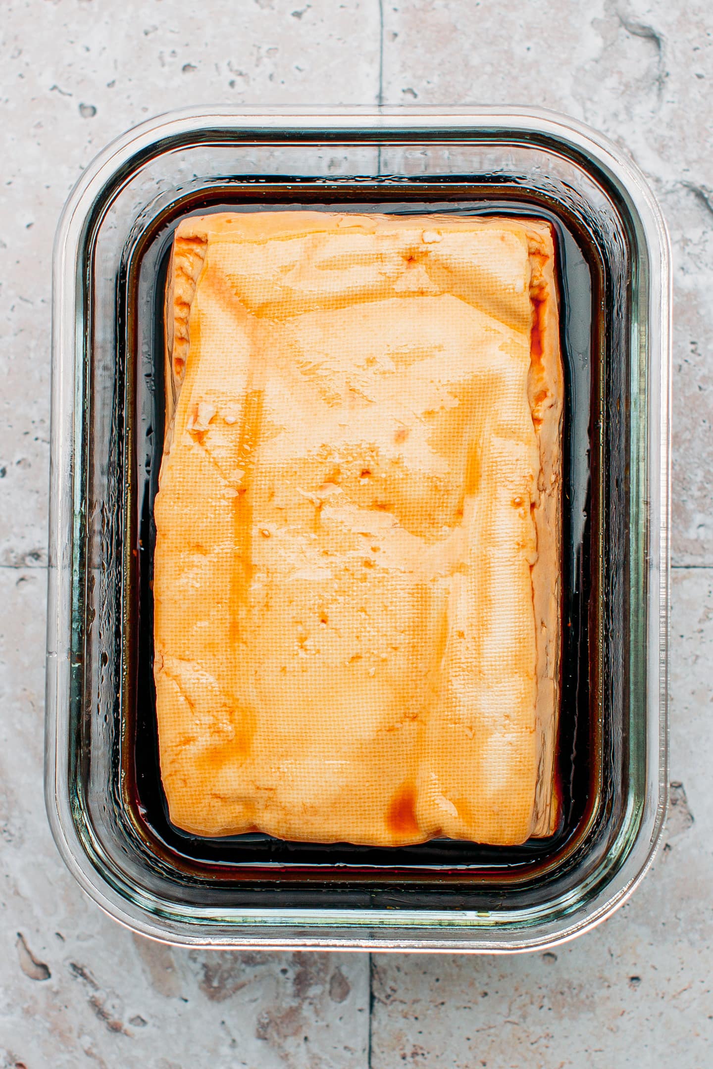 Tofu marinated with soy sauce and maple syrup in a glass dish.