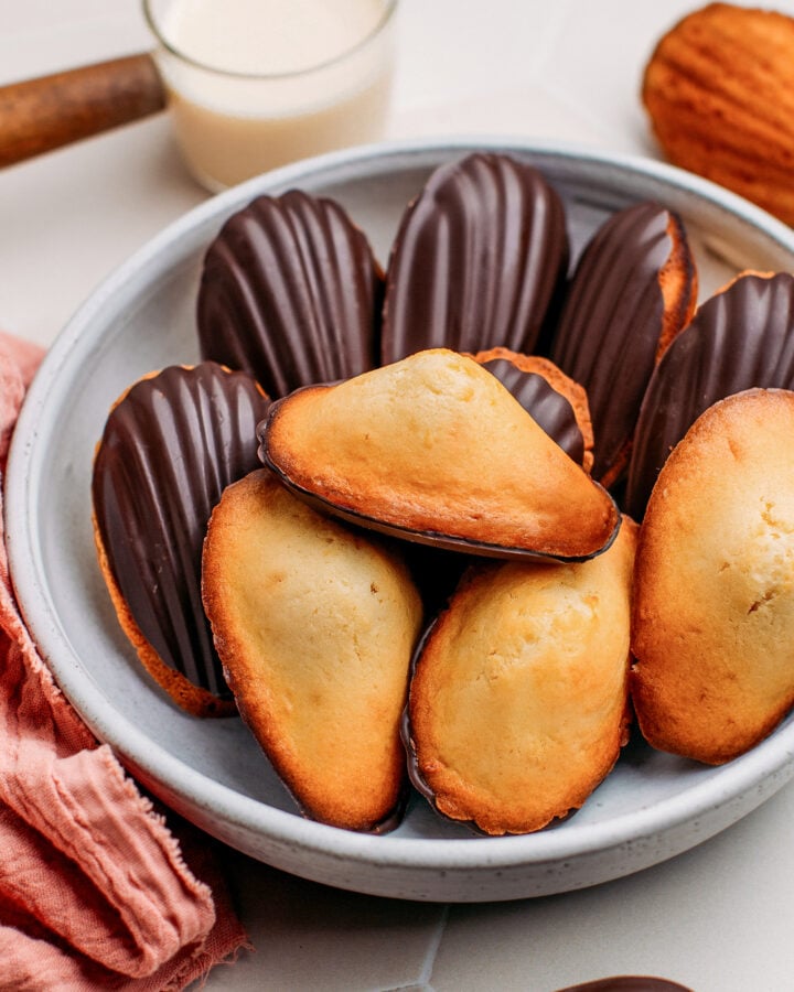 Vegan madeleines dipped in dark chocolate on a plate.