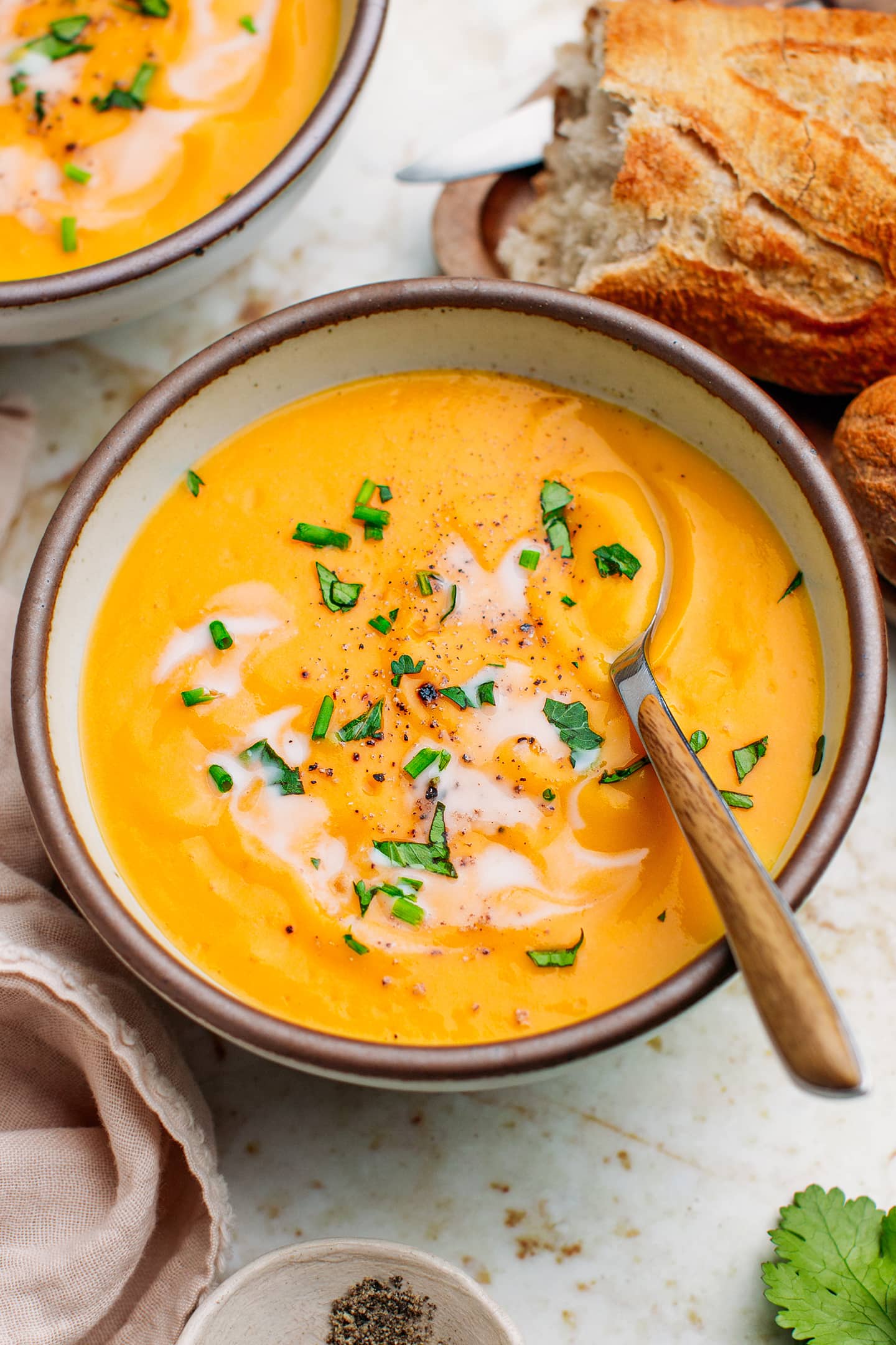 Butternut squash soup in a bowl topped with chopped cilantro and ground black pepper.