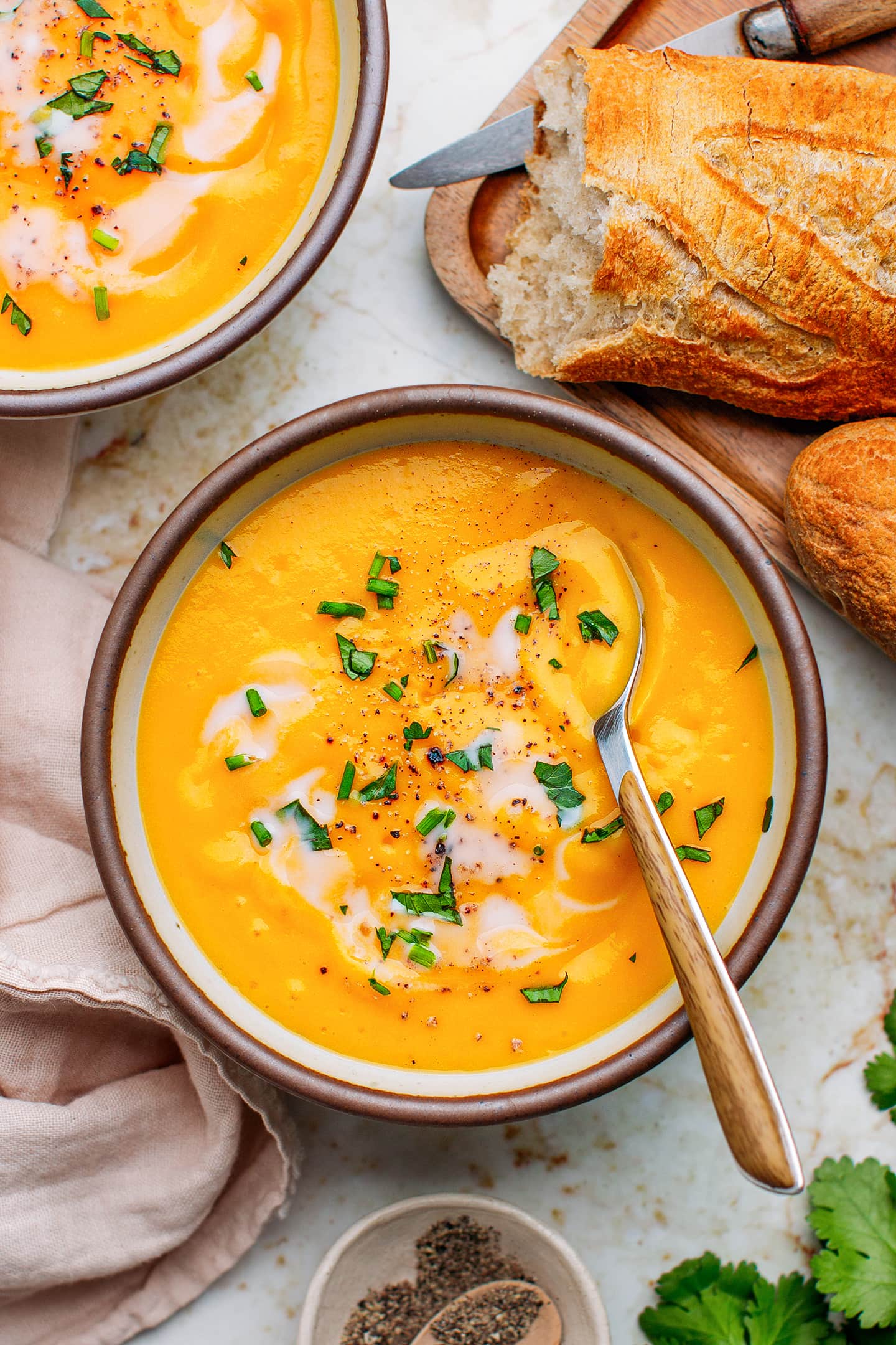 Two bowls of butternut squash soup with a loaf of baguette on the side.