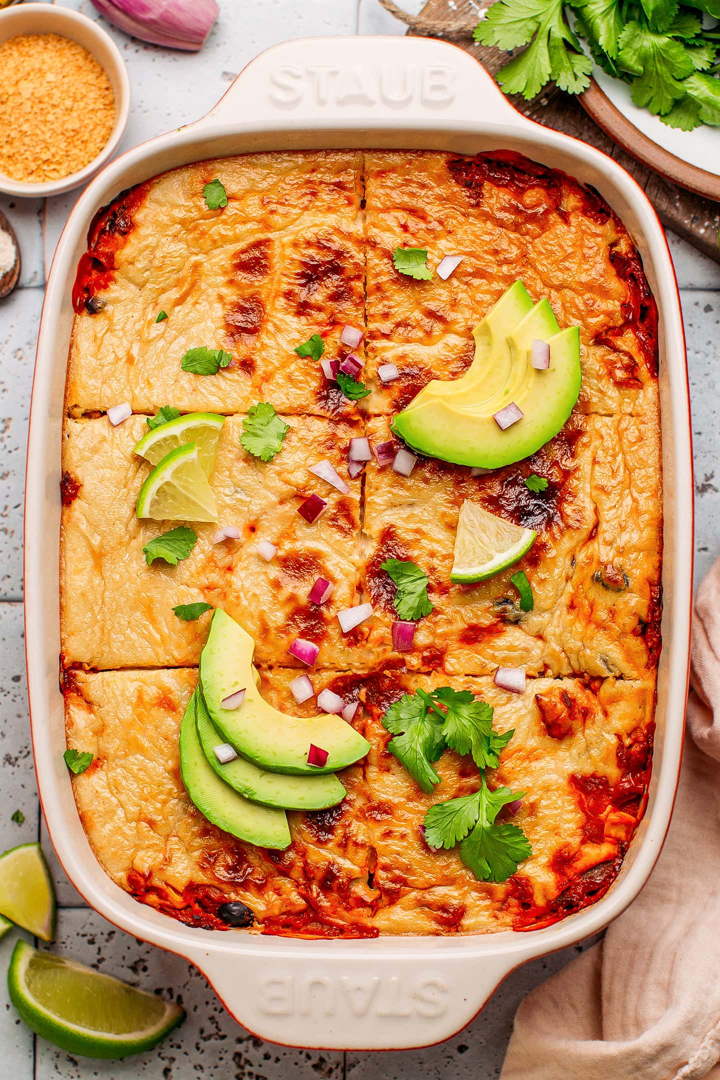 Enchilada casserole topped with avocado, red onion, and cilantro.