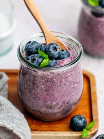 Blueberry oats with fresh blueberries and basil leaves in a small jar.