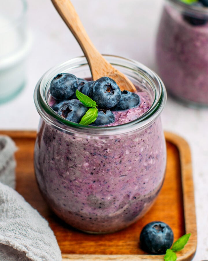 Blueberry oats with fresh blueberries and basil leaves in a small jar.