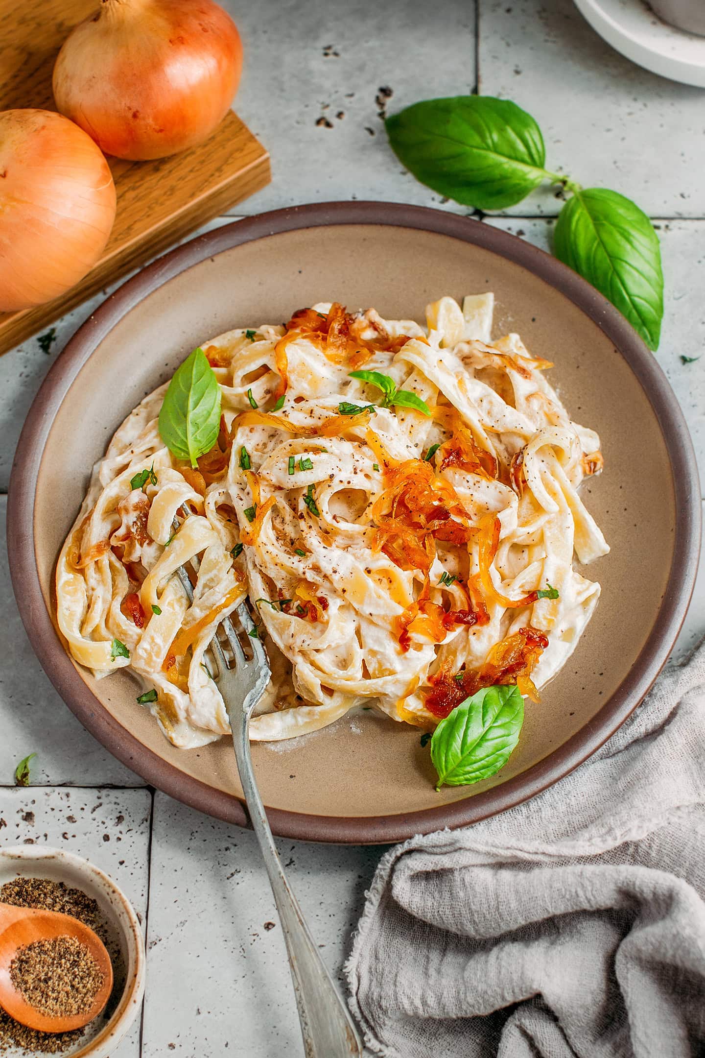 Caramelized onion pasta topped with onions and basil leaves on a brown plate.