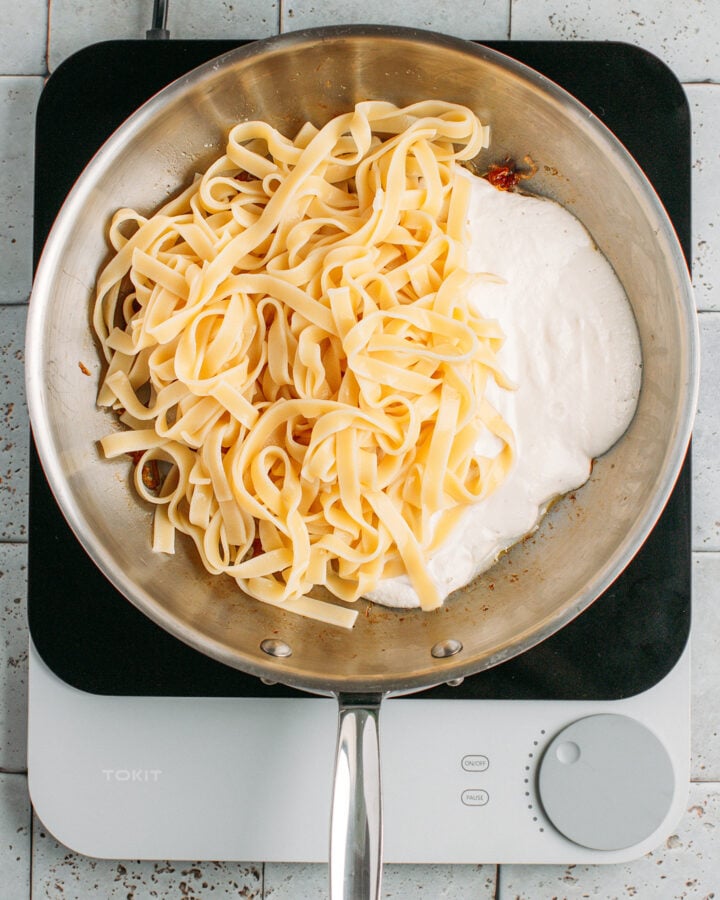 Caramelized onions, cooked pasta, and cashew cream in a skillet.