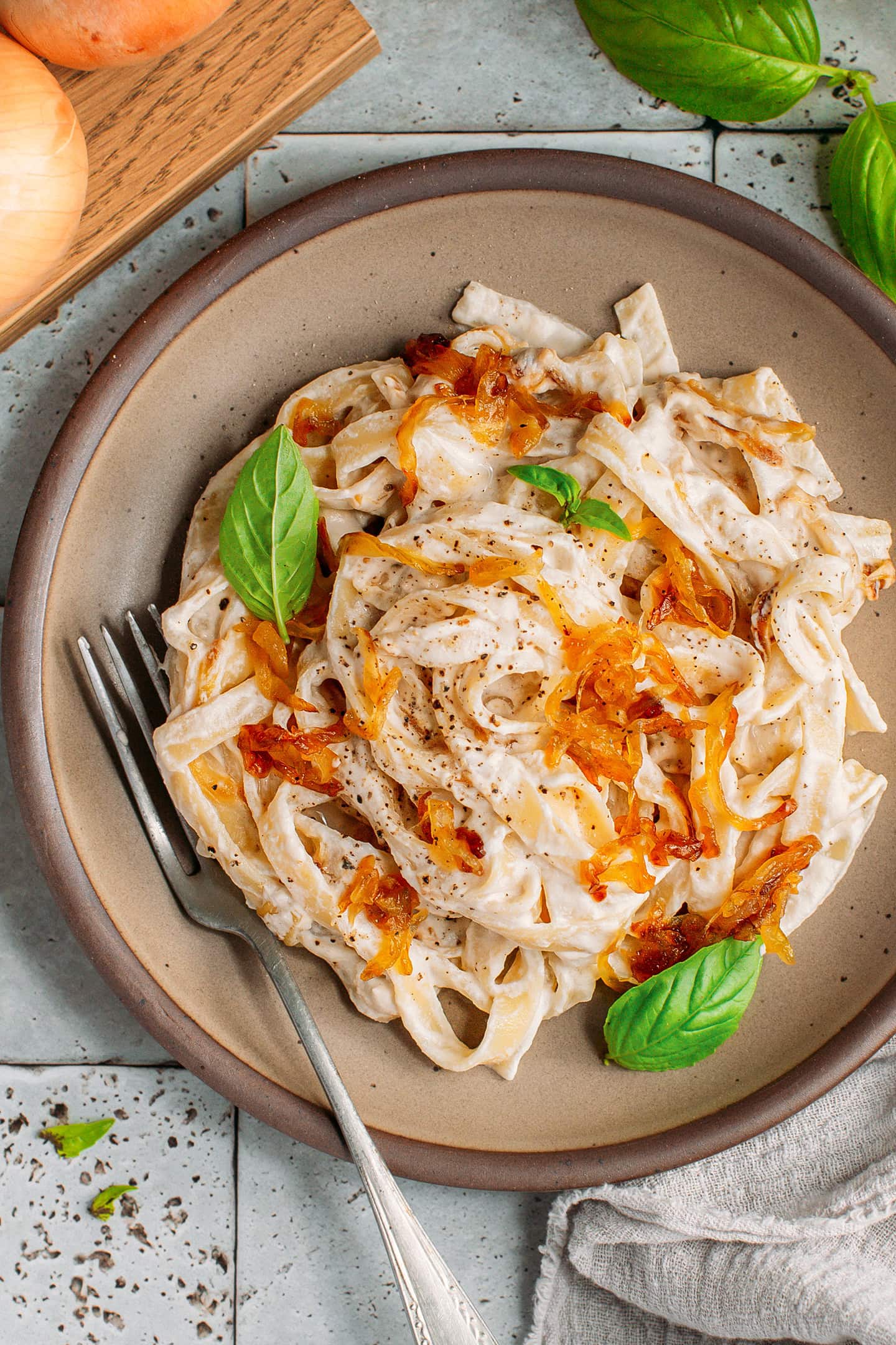 Long pasta tossed with cashew cream and caramelized onions on a brown plate.