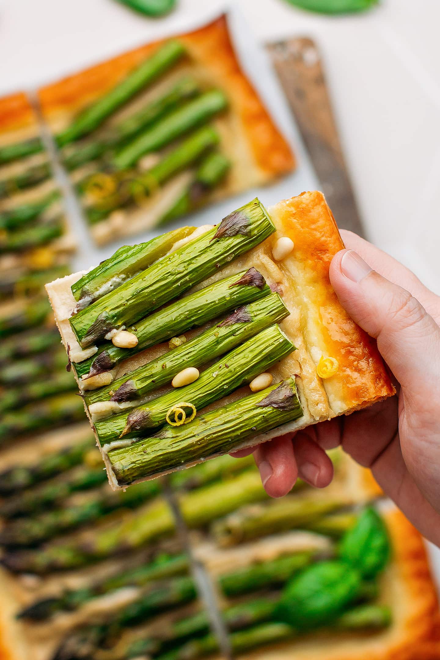 Holding a slice of asparagus tart topped with pine nuts and lemon zest.