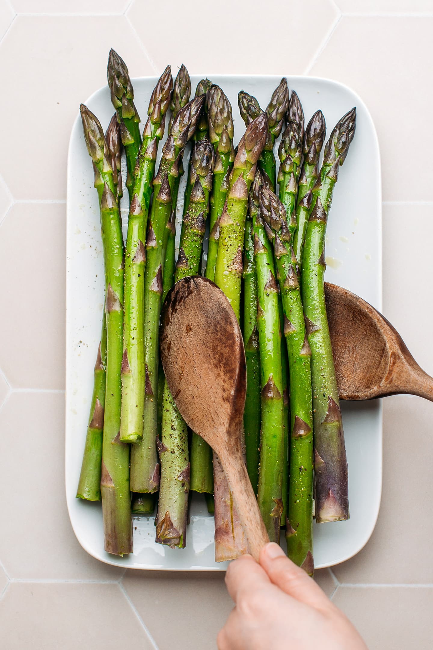 Tossing green asparagus with olive oil, salt, and pepper.