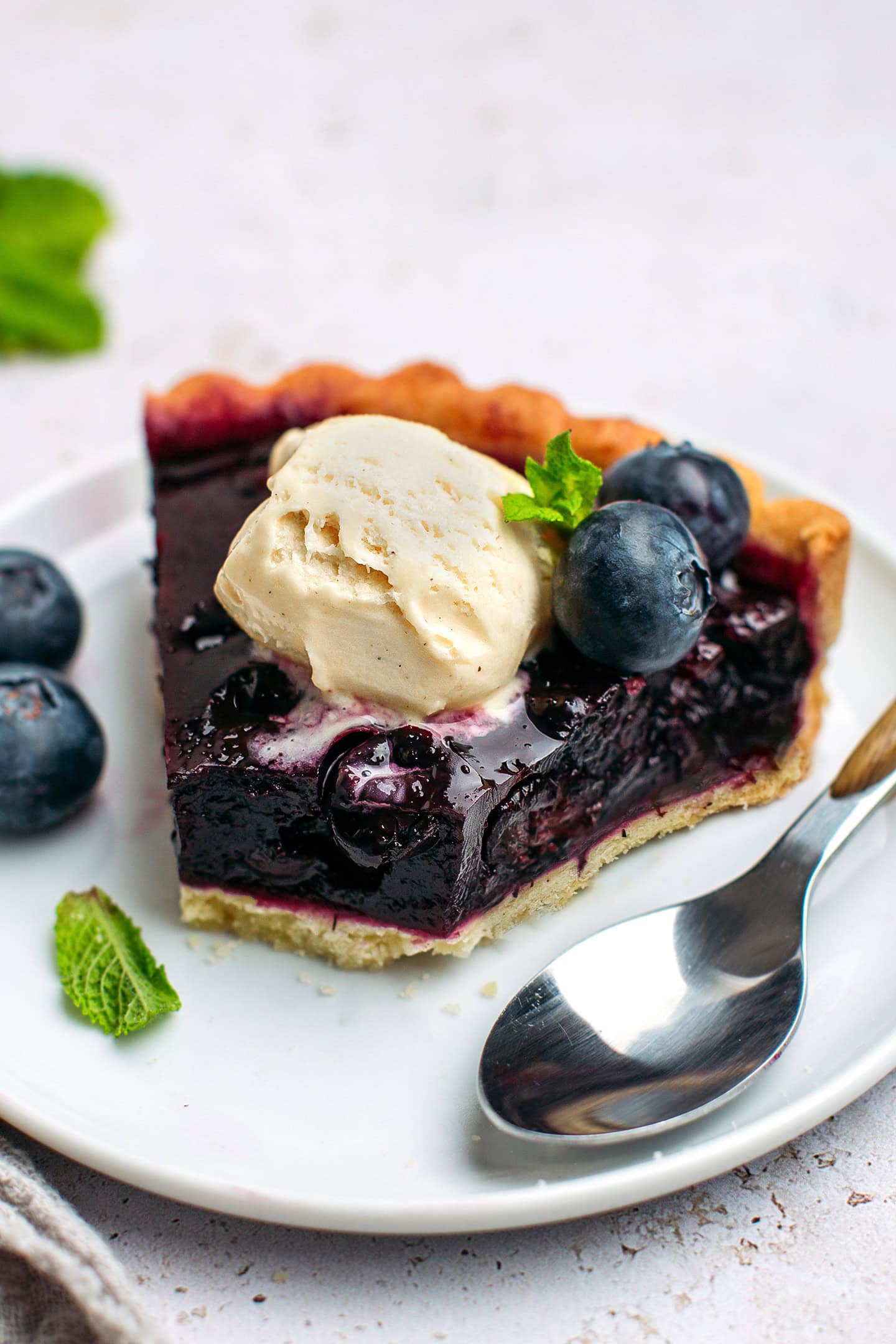 Slice of blueberry tart topped with vanilla ice cream.