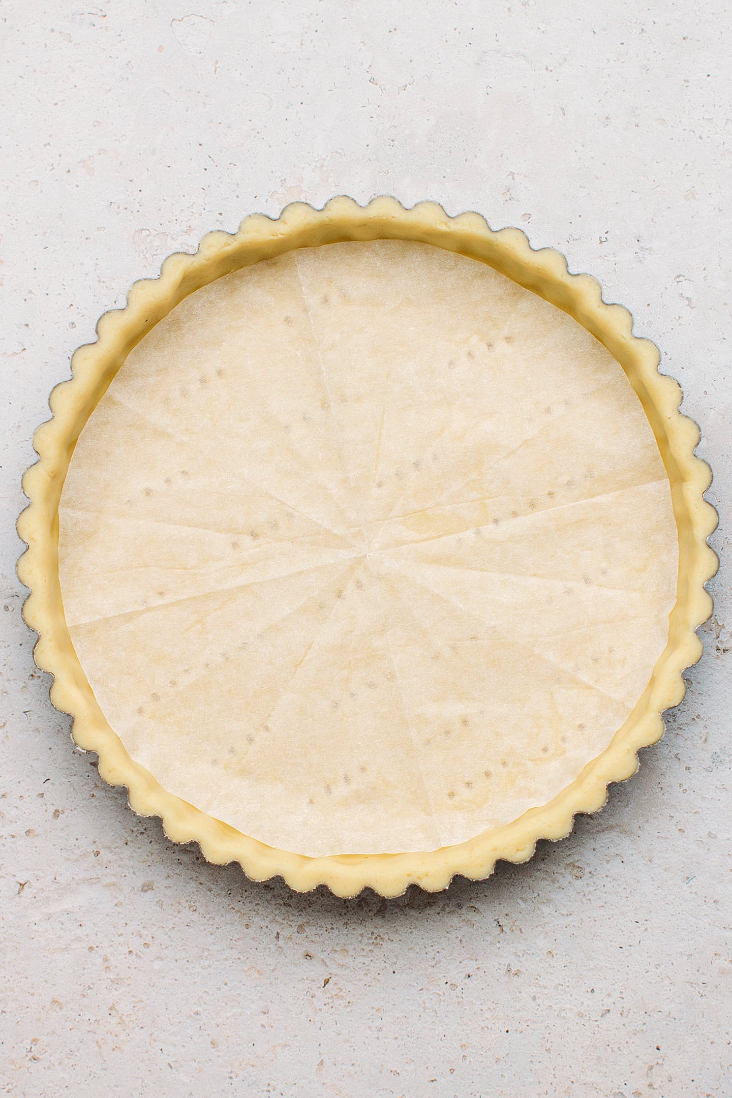 Shortcrust pastry in a pie pan topped with parchment paper.