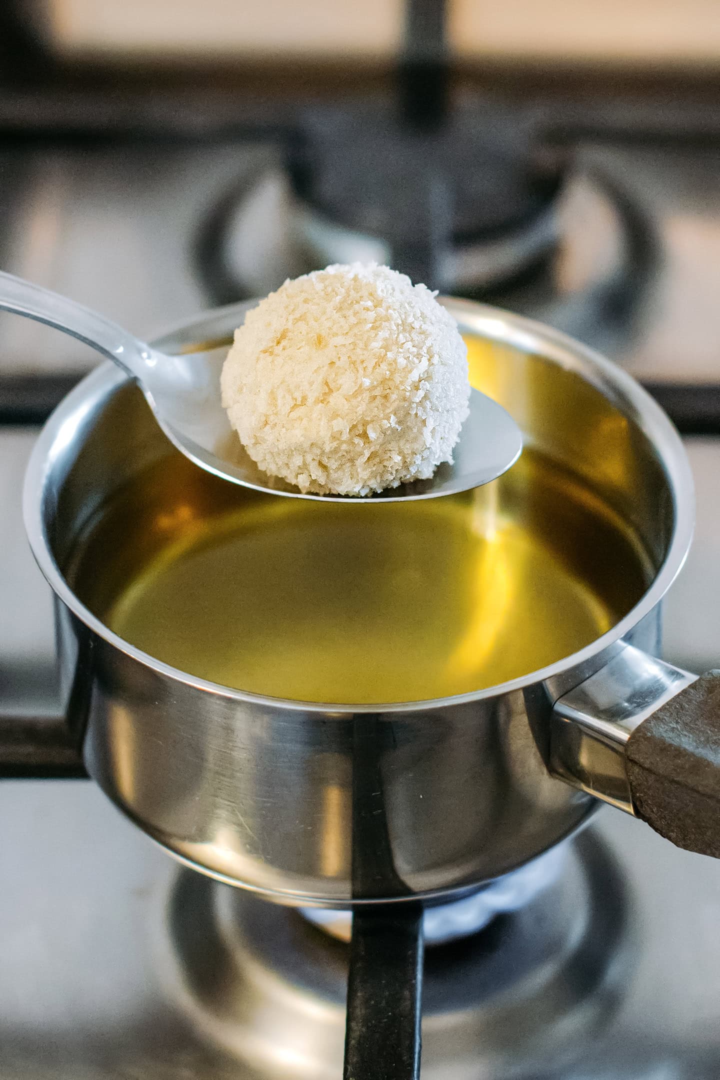 Holding a ball of cashew cheese coated with breadcrumbs over a pot of oil.