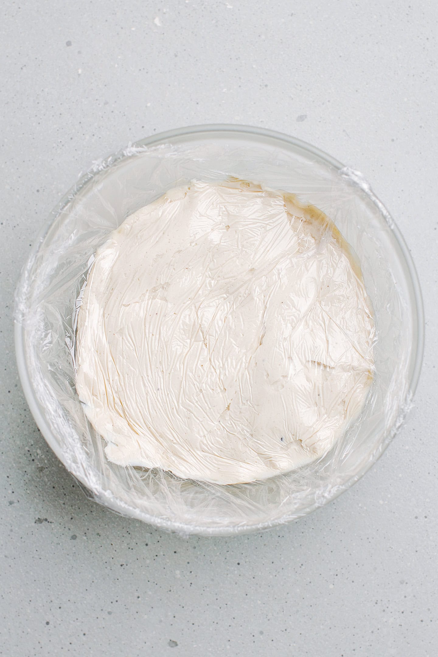 Cashew cream cheese covered with plastic wrap in a bowl.