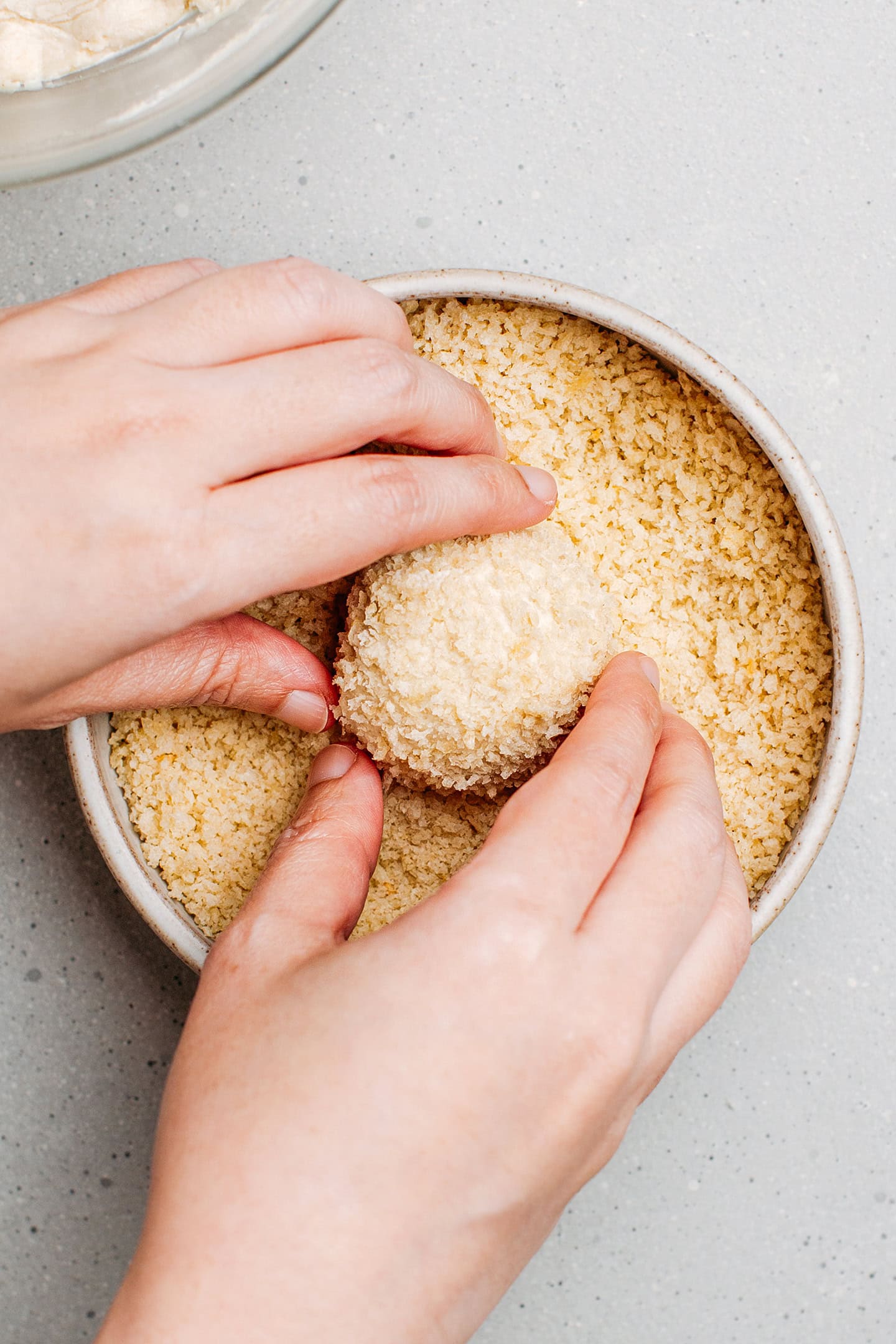 Coating a vegan cheese ball with breadcrumbs.