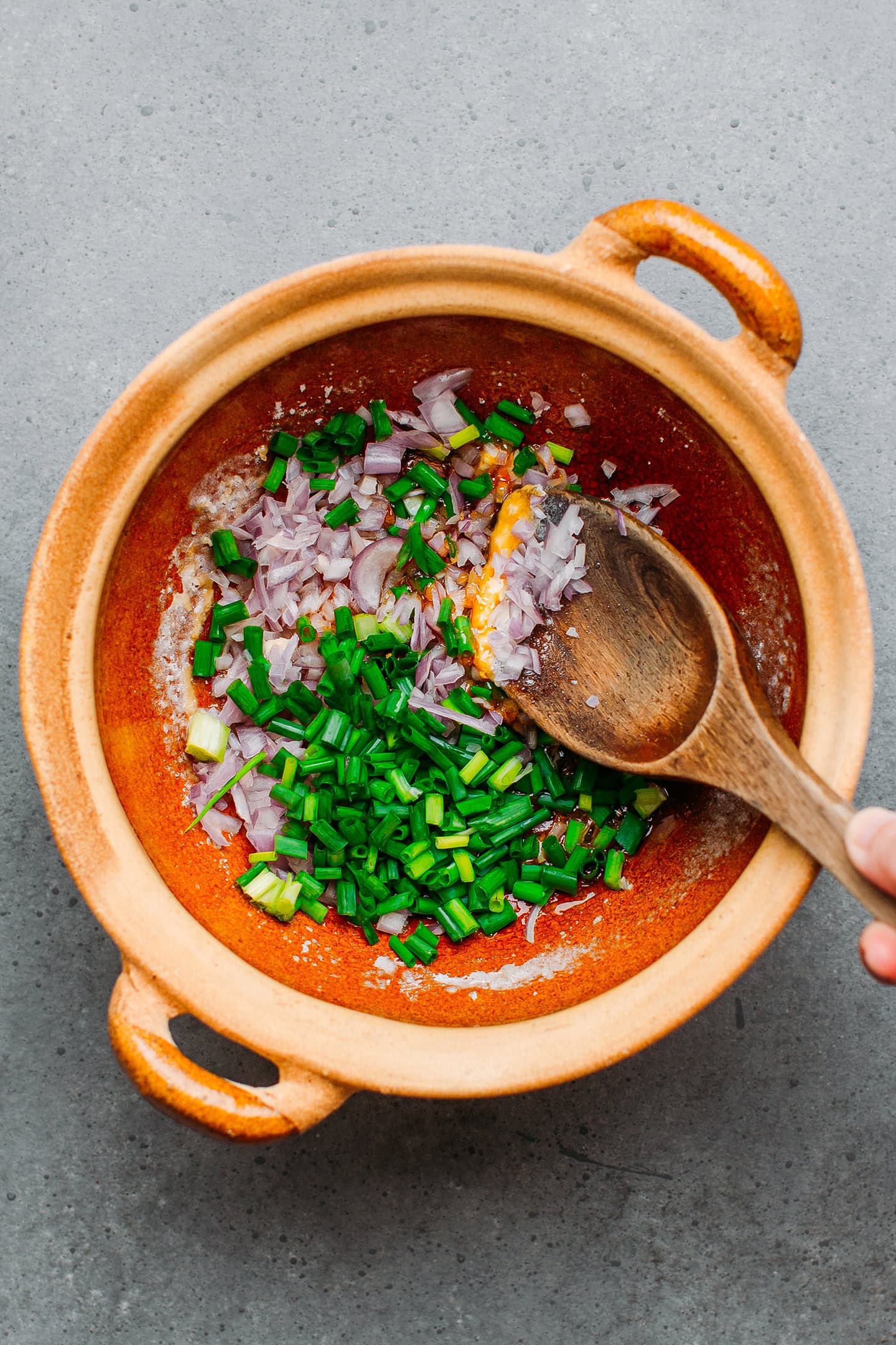 Stirring shallots and green onions in a clay pot.