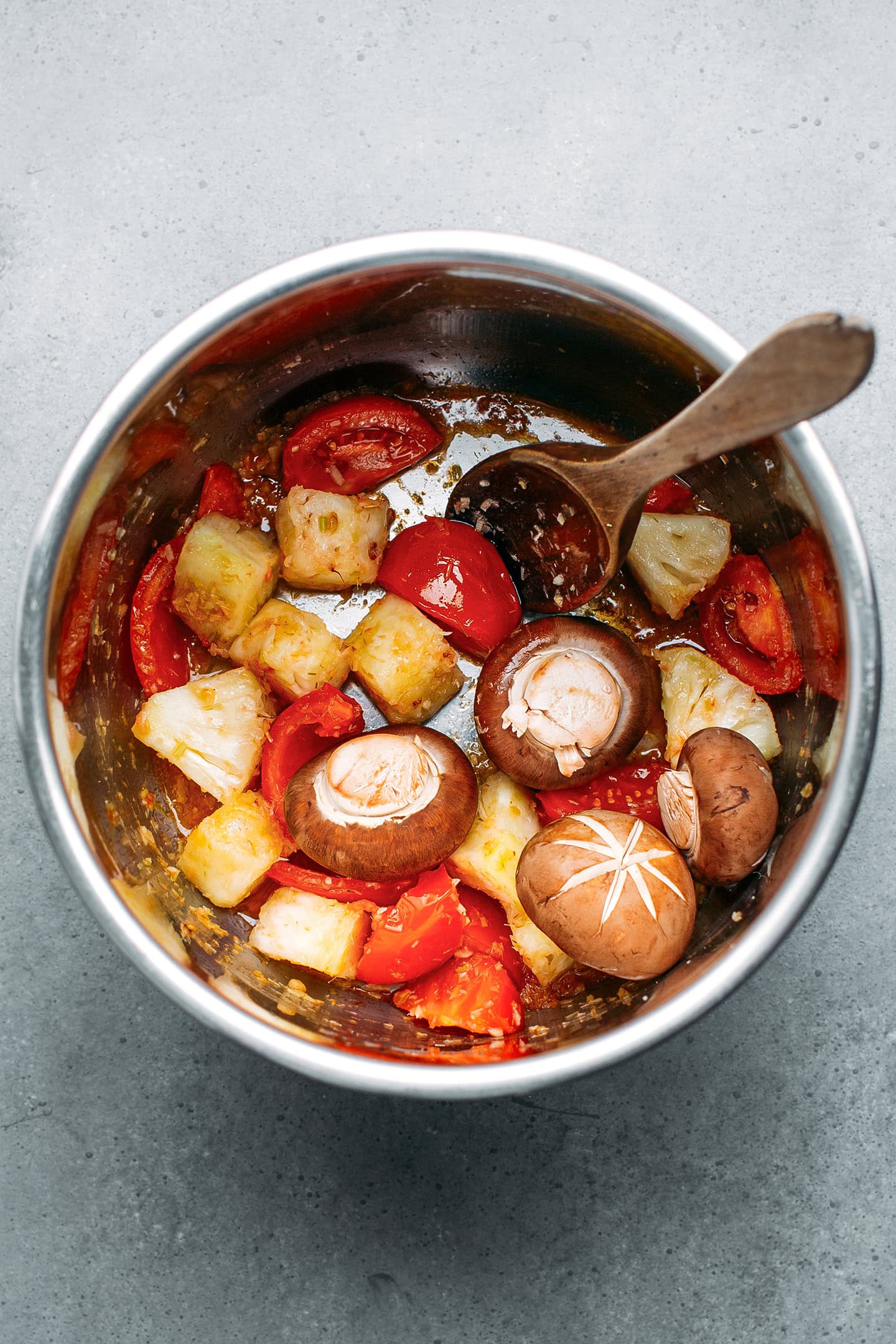 Chopped pineapple, tomatoes, and mushrooms in a pot.