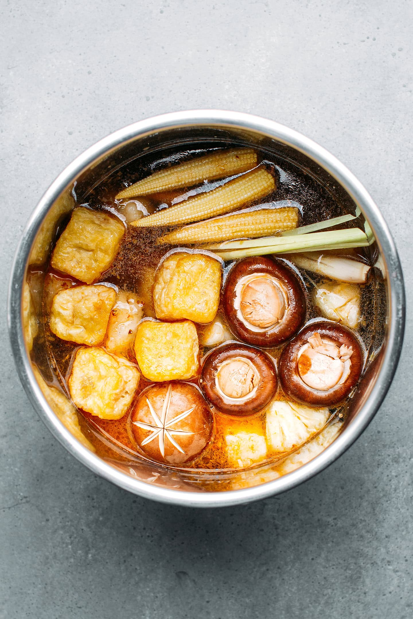 Tofu puffs, lemongrass stalks, mushrooms, and pineapple in a pot.