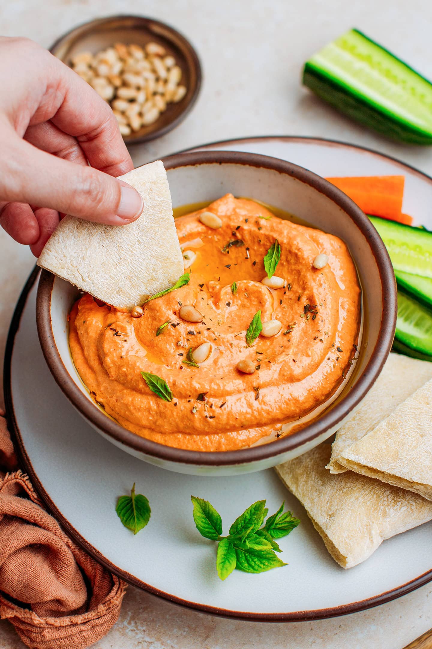 Red bell pepper dip topped with toasted pine nuts and mint leaves in a bowl.