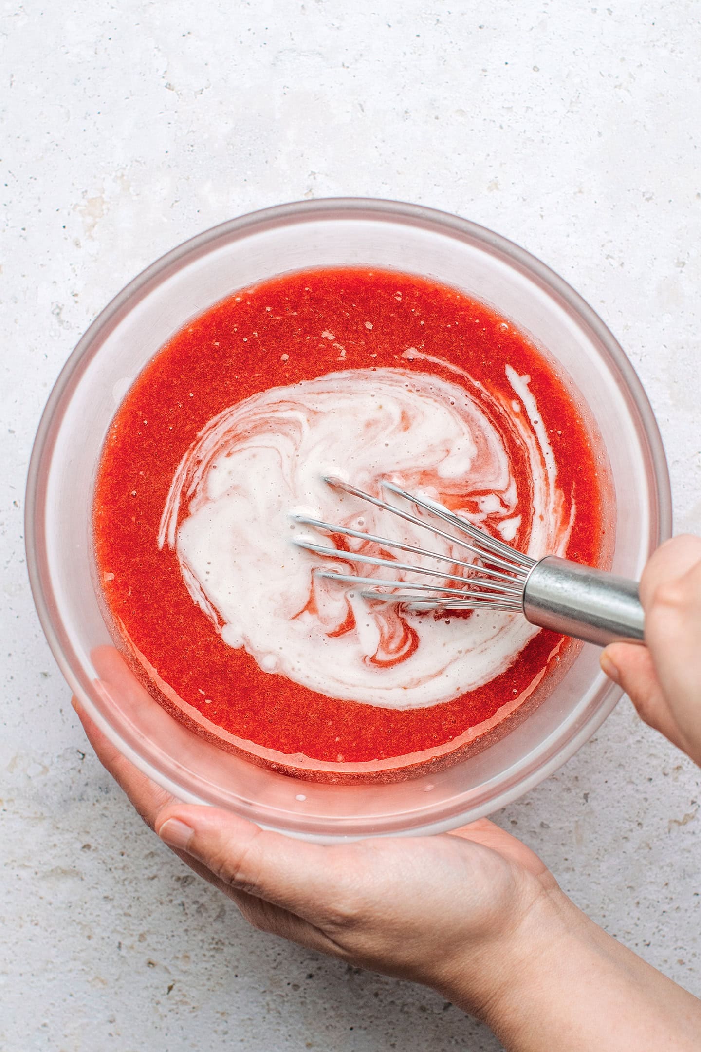 Whisking strawberry juice with coconut cream in a bowl.