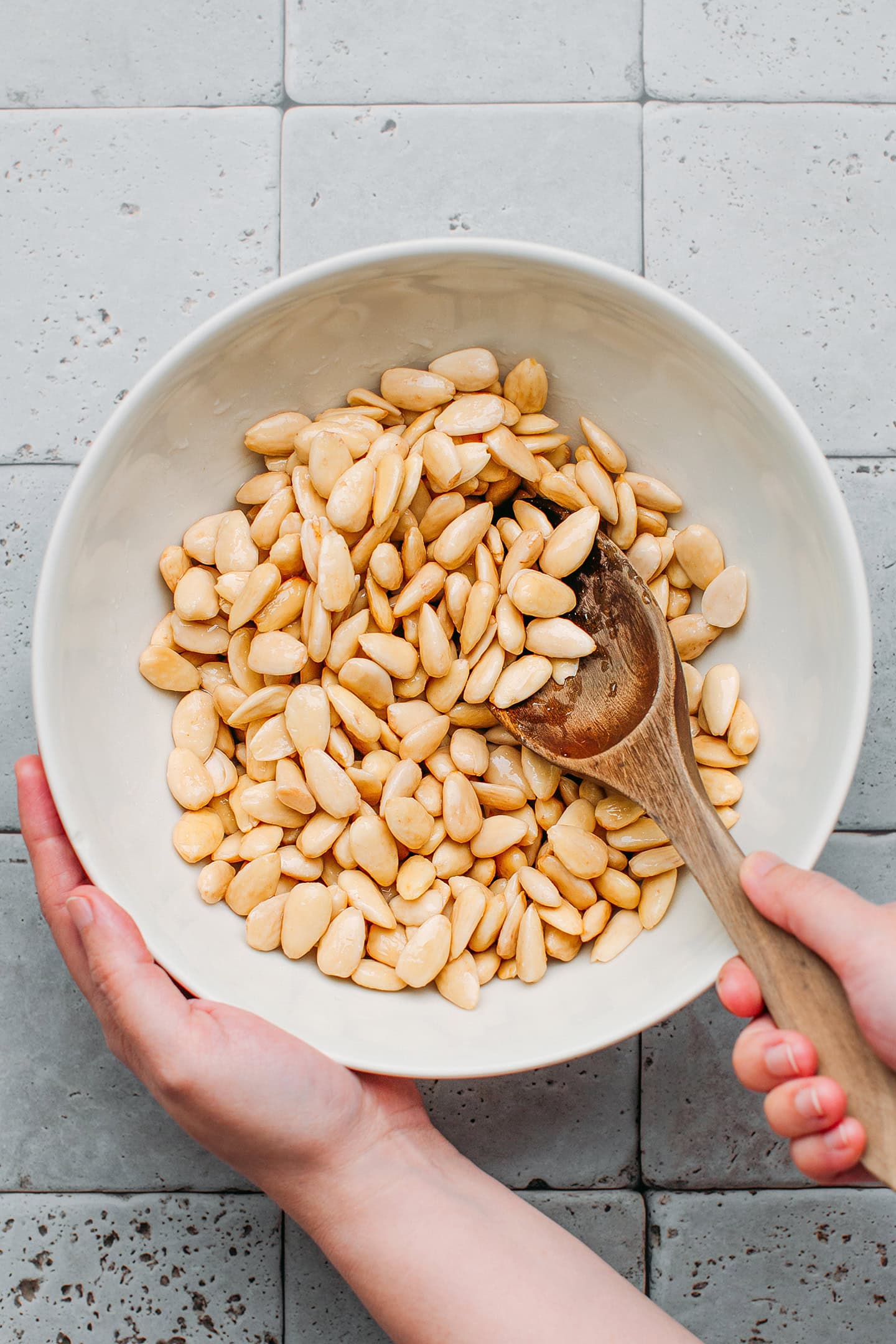 Stirring blanched almonds with syrup in a bowl.