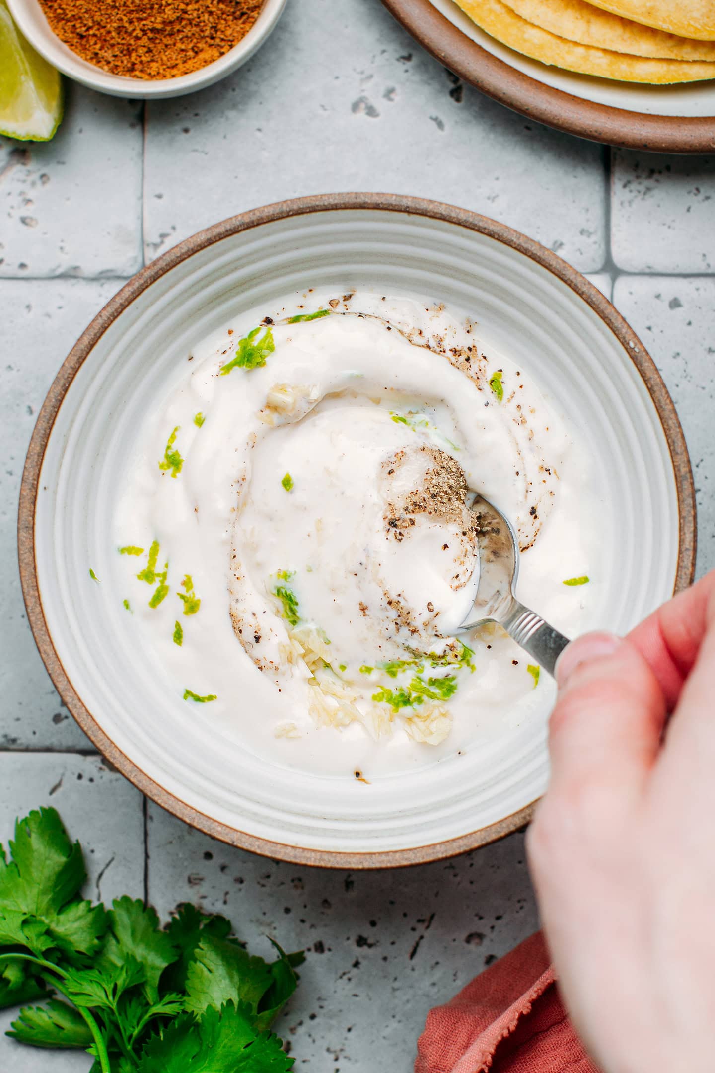 Stirring yogurt with lime zest, pepper, and garlic in a bowl.