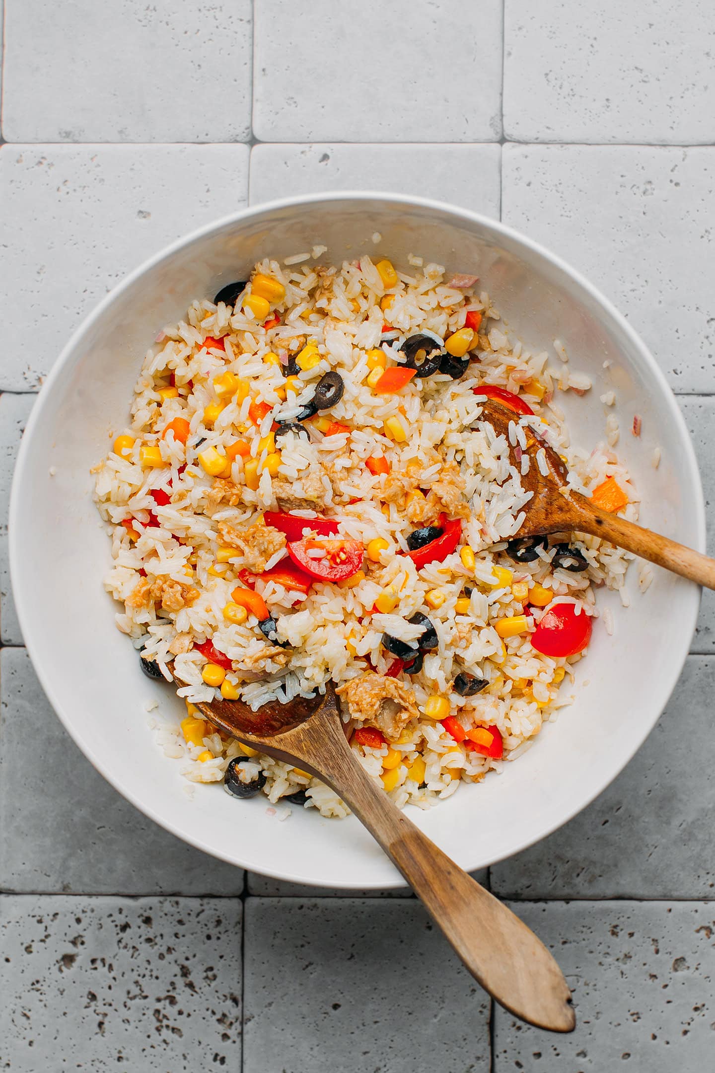 Vegan rice salad with olives and tomatoes in a mixing bowl.