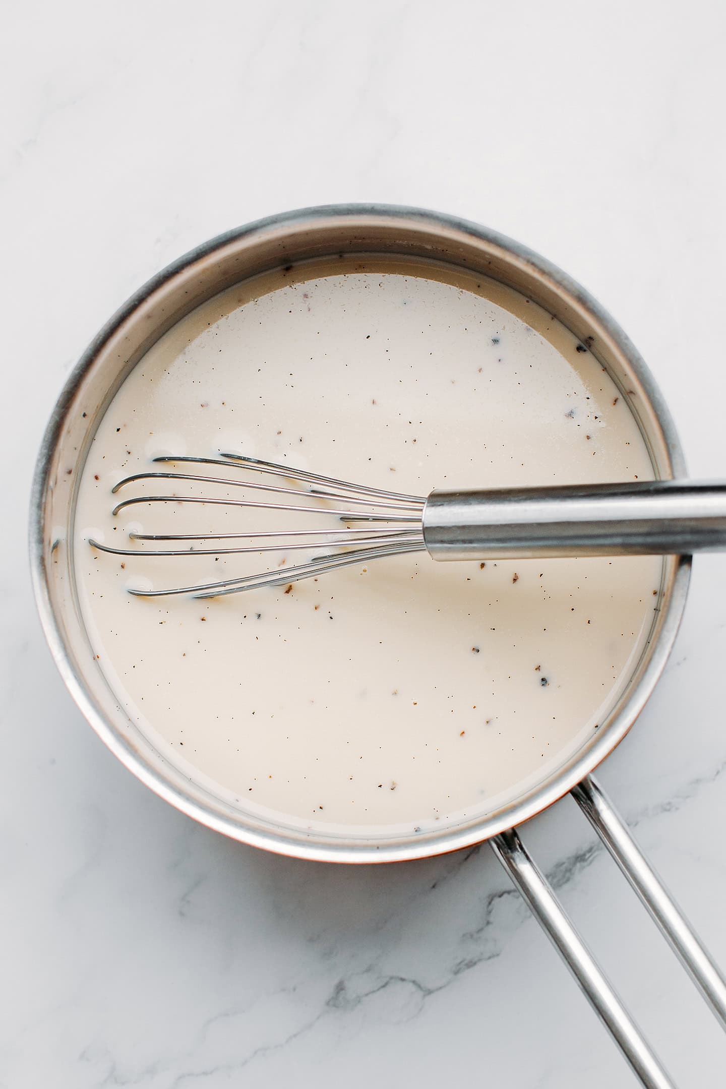 Whisking plant-based milk with vanilla seeds and cornstarch in a saucepan.