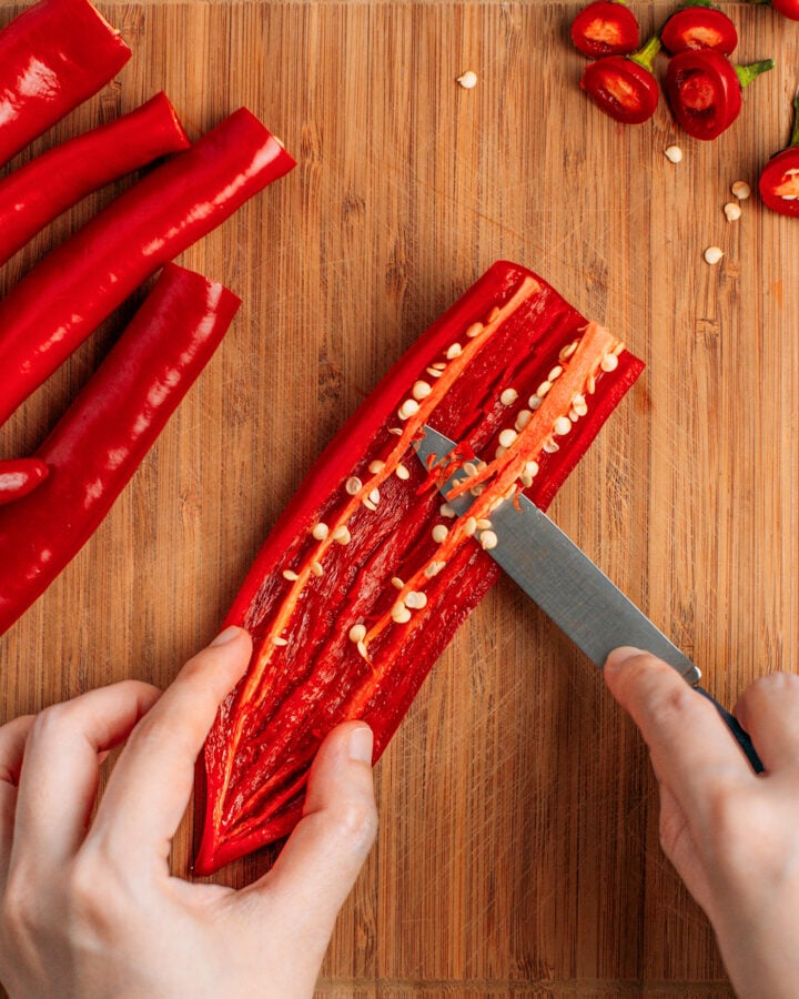 Using a knife to remove the seeds and stems from a chili.
