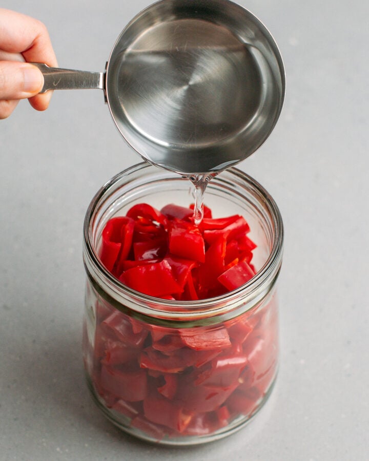 Pouring brine into a jar filled with chopped cayenne peppers.