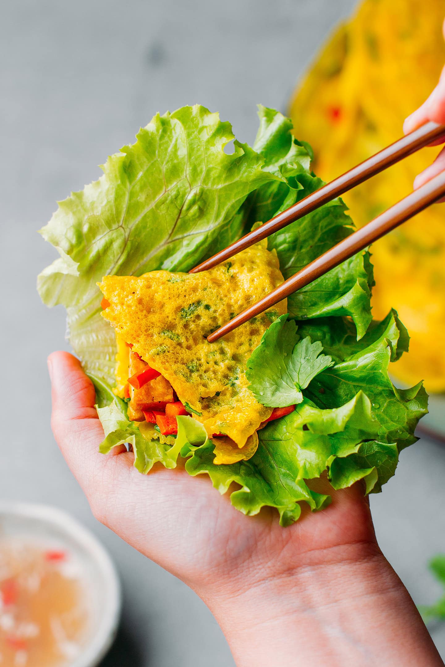 Placing a piece of bánh xèo on a leaf of salad.