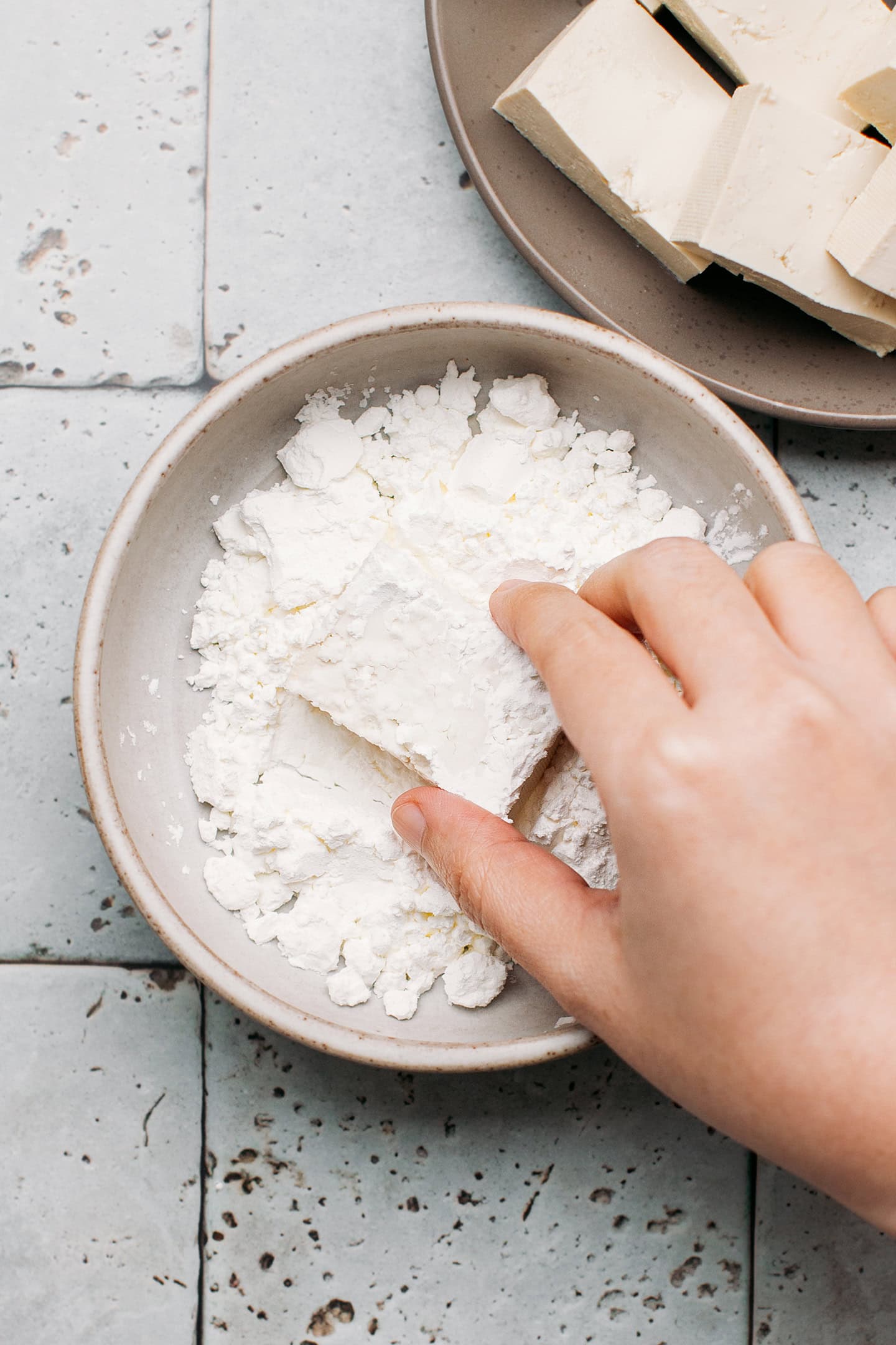 Coating a piece of tofu with cornstarch.