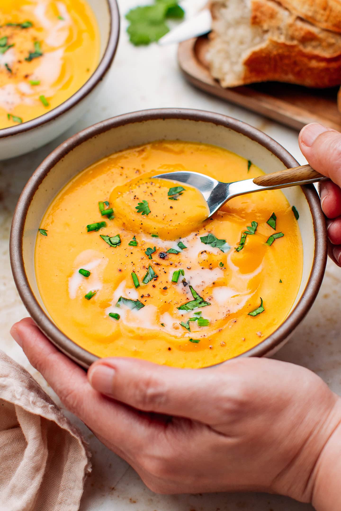 Holding a bowl of butternut squash soup topped with cilantro and ground black pepper.