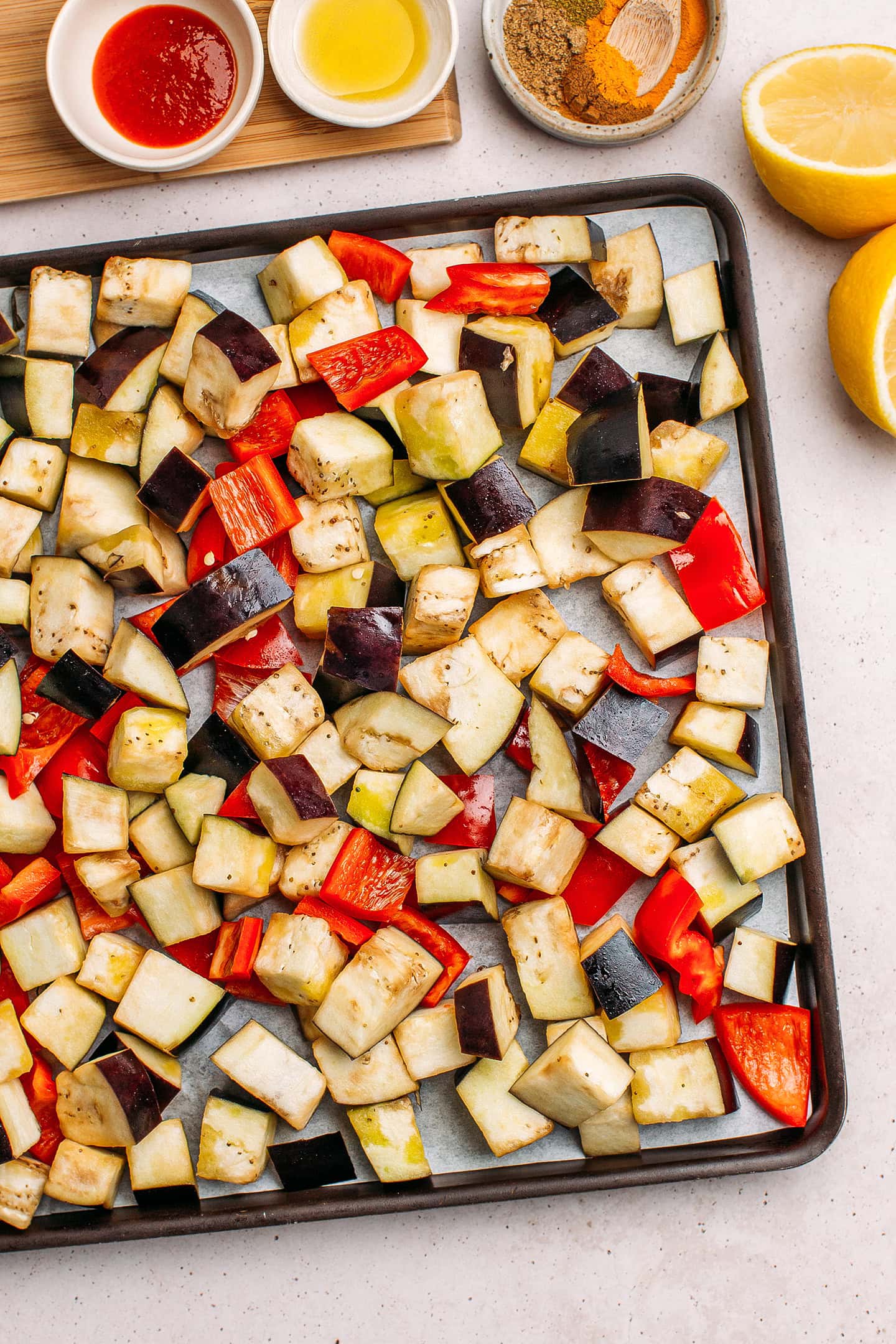 Diced eggplant and red bell pepper on a baking sheet.