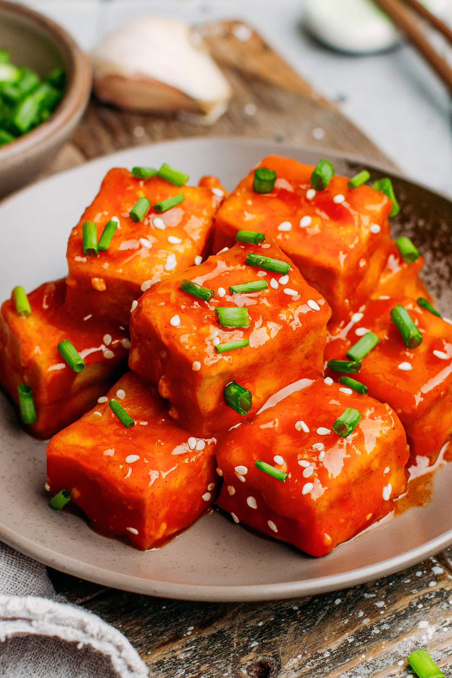 Close-up of diced tofu coated with a gochujang sauce and topped with green onions and sesame seeds.