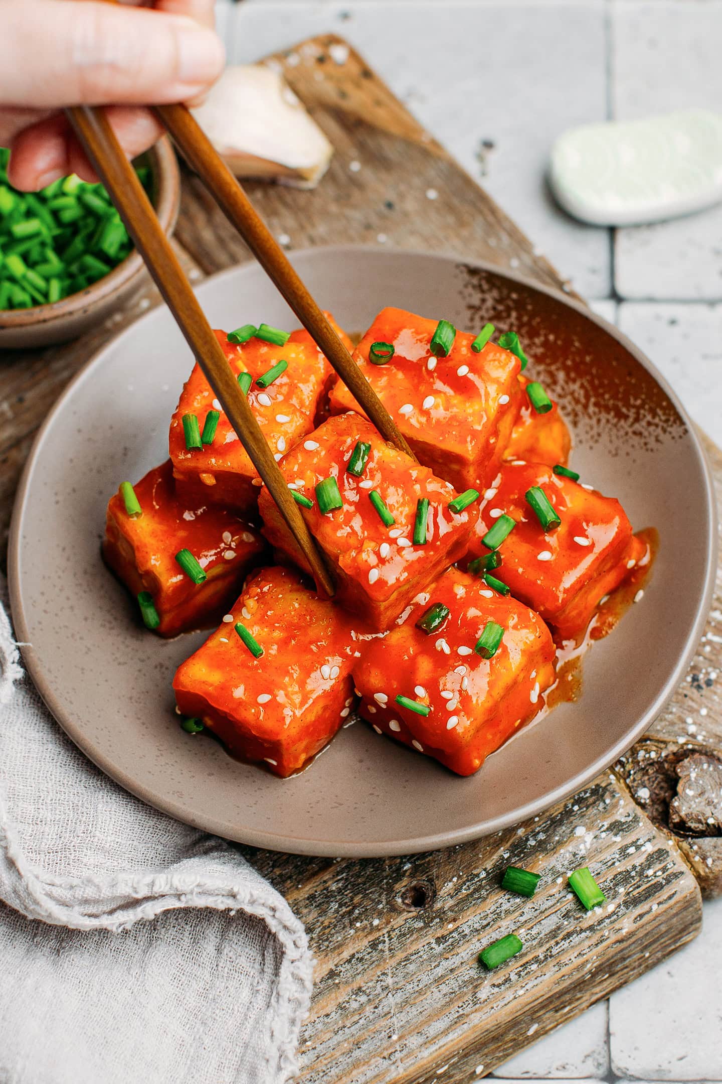 Picking a piece of gochujang tofu using chopsticks.