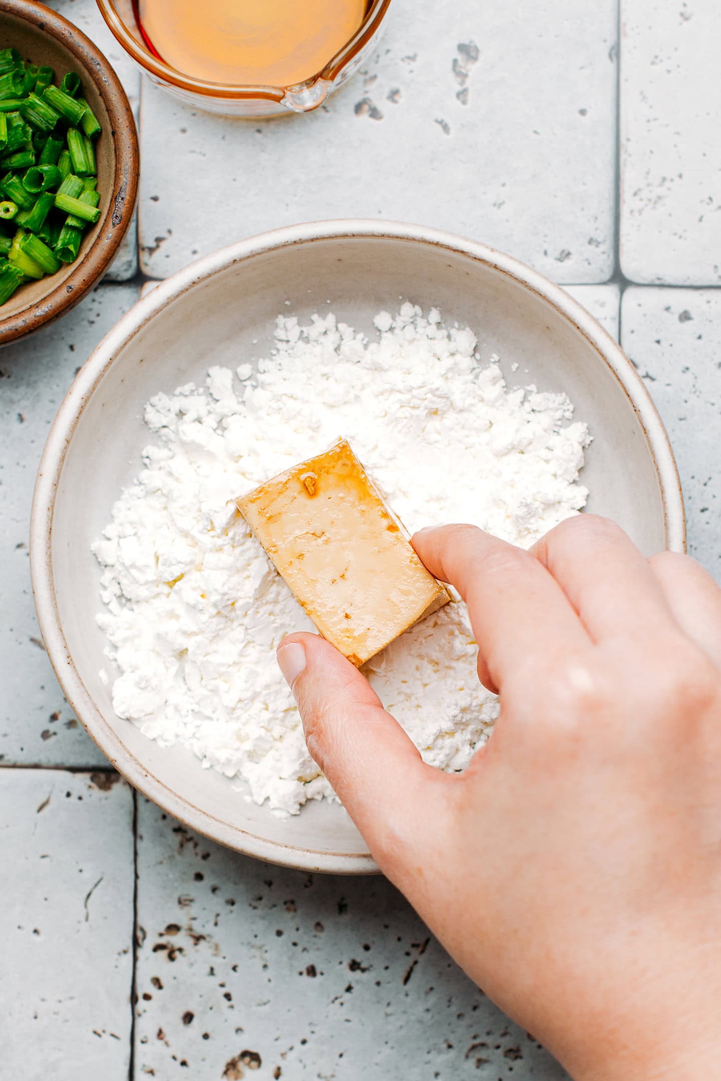 Coating a piece of tofu with cornstarch.