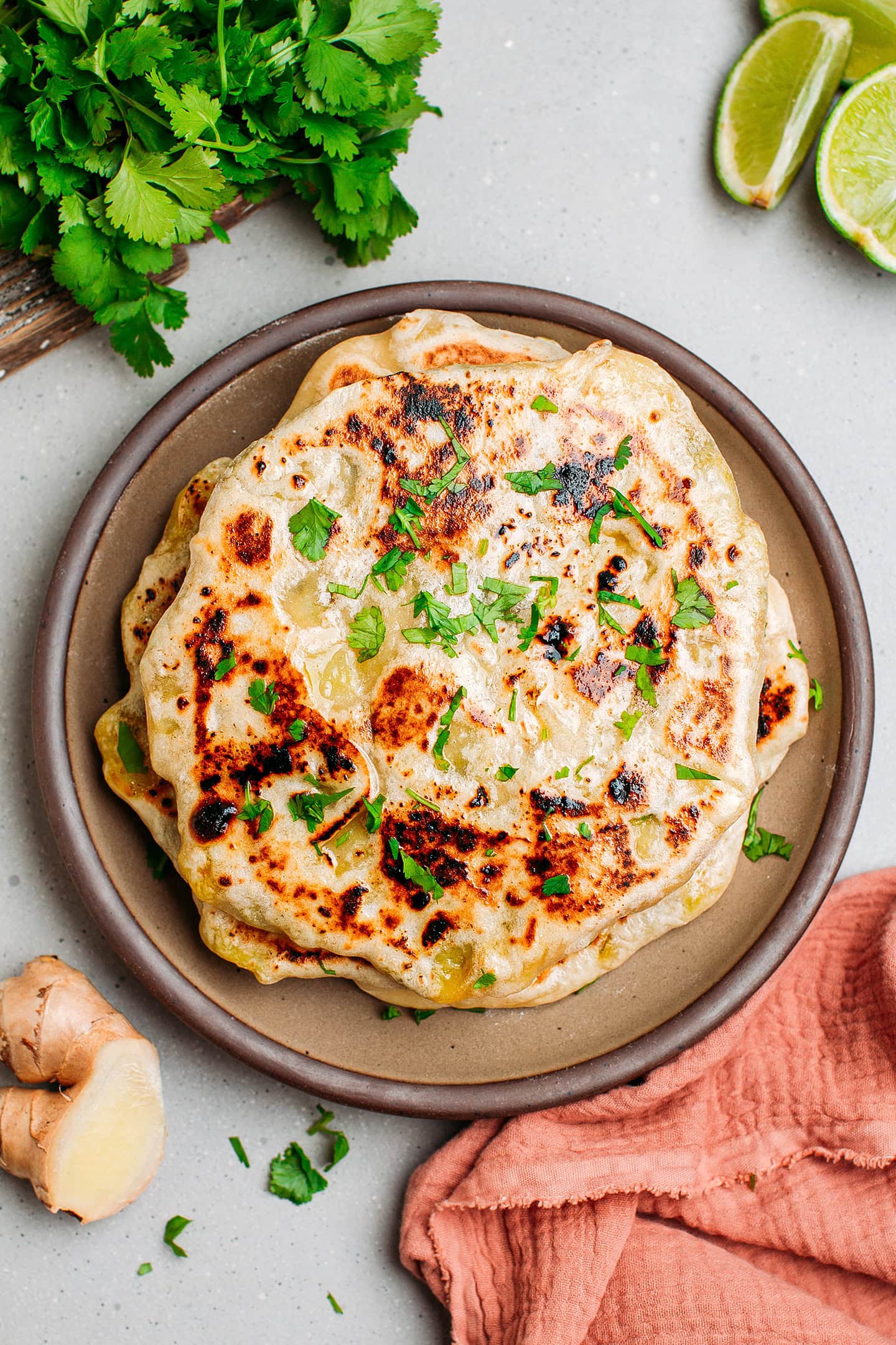 Naan topped with cilantro and stacked on a plate.