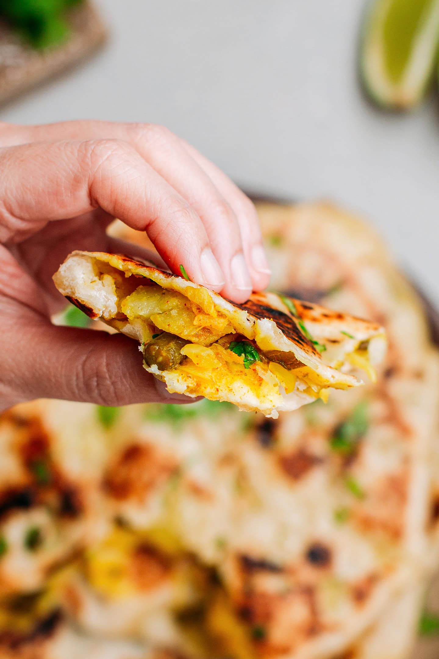 Holding a piece of naan stuffed with potatoes and green beans.