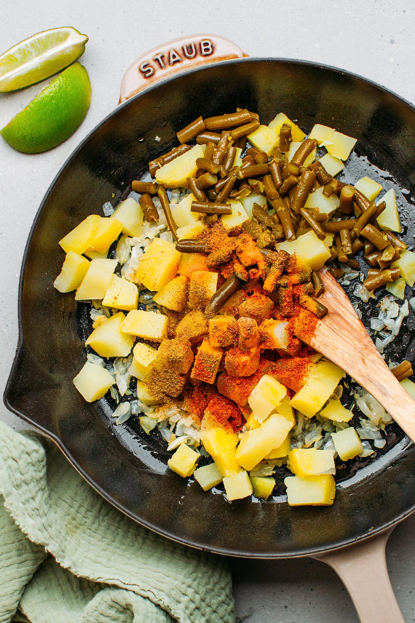 Diced potatoes, green beans, and spices in a skillet.