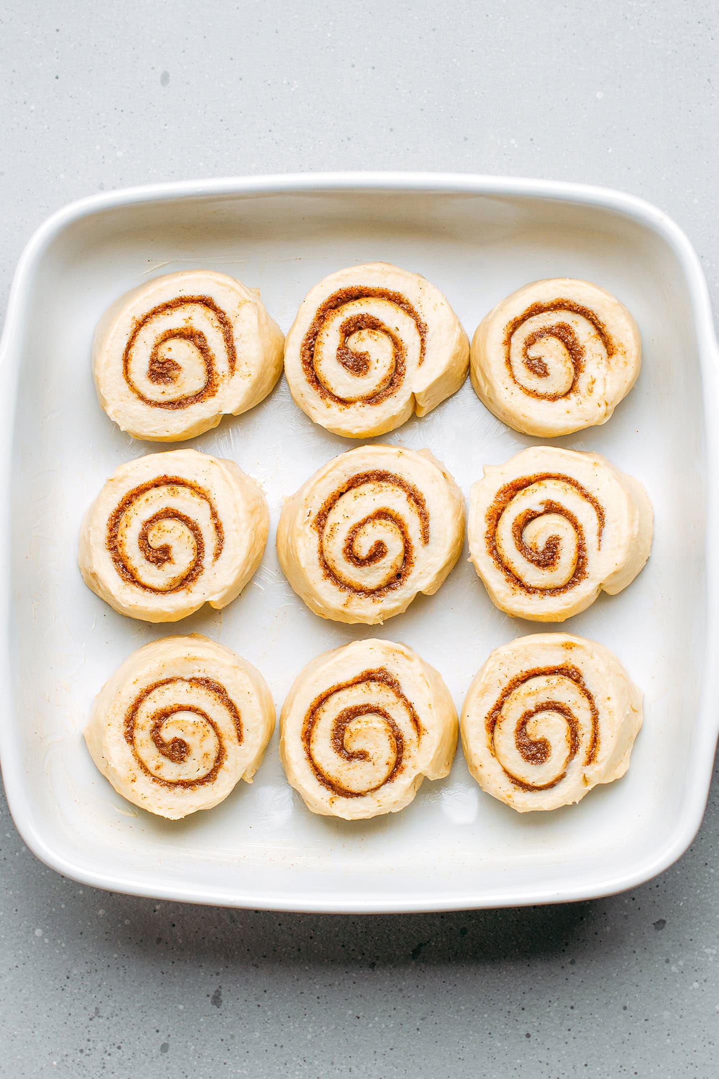 Unbaked cinnamon rolls in a square baking dish.