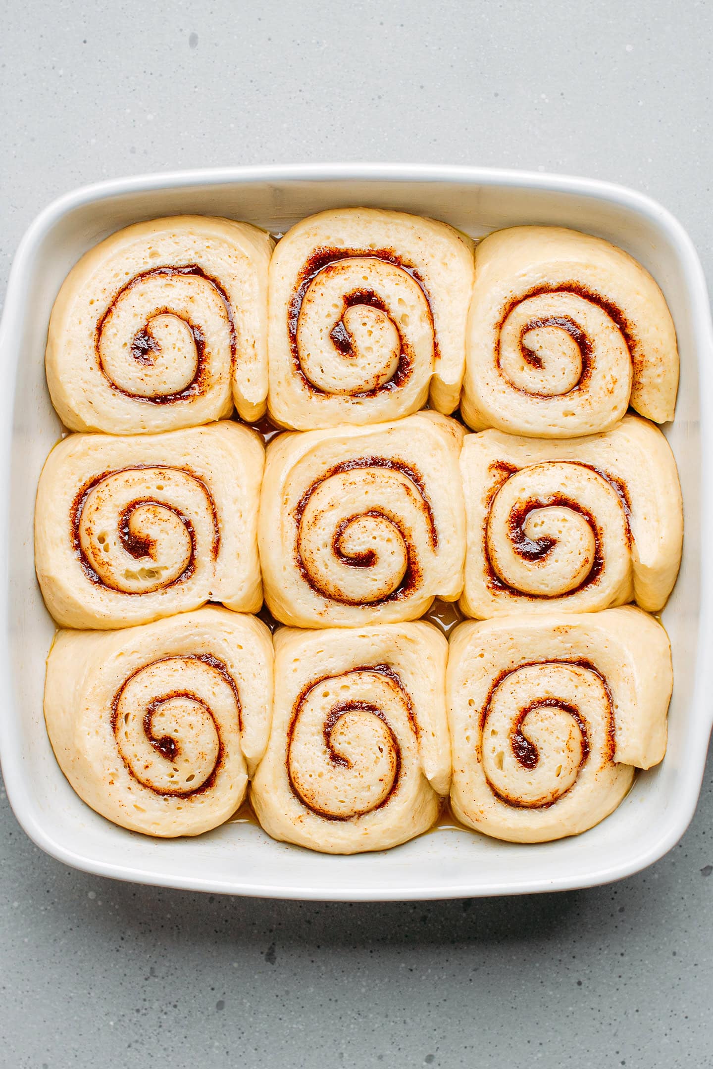 Unbaked cinnamon rolls after rising in a square baking dish.