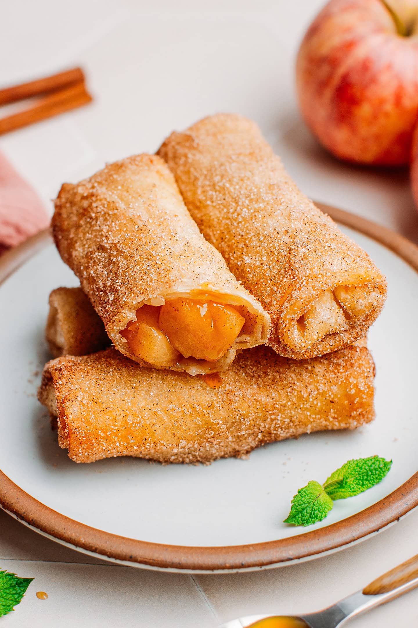 Four apple egg rolls stacked on a plate.