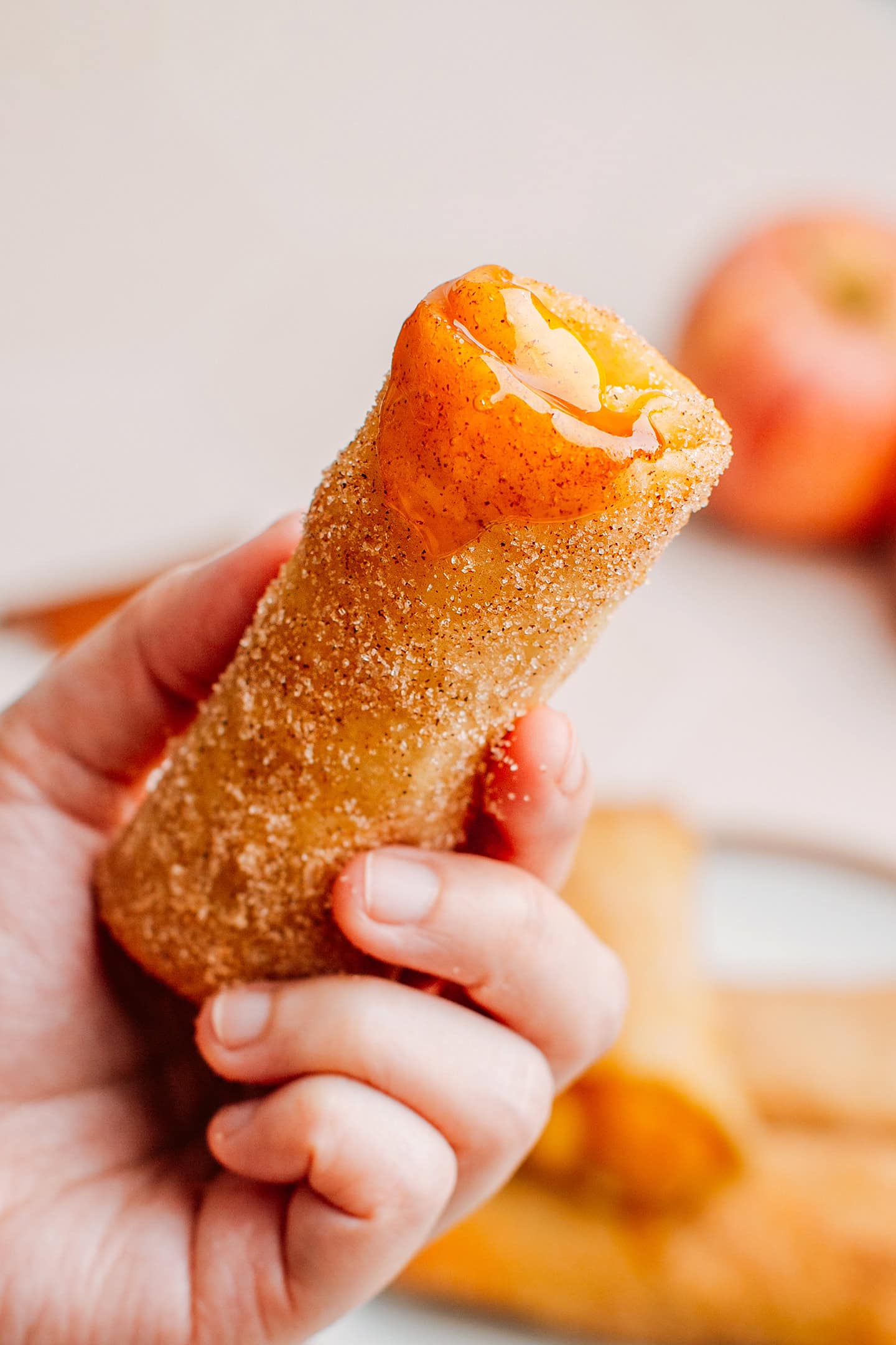 Holding an apple egg roll dipped in caramel sauce.