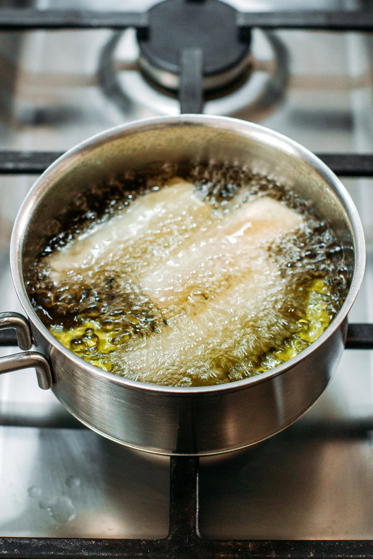 Apple egg rolls frying in a saucepan.