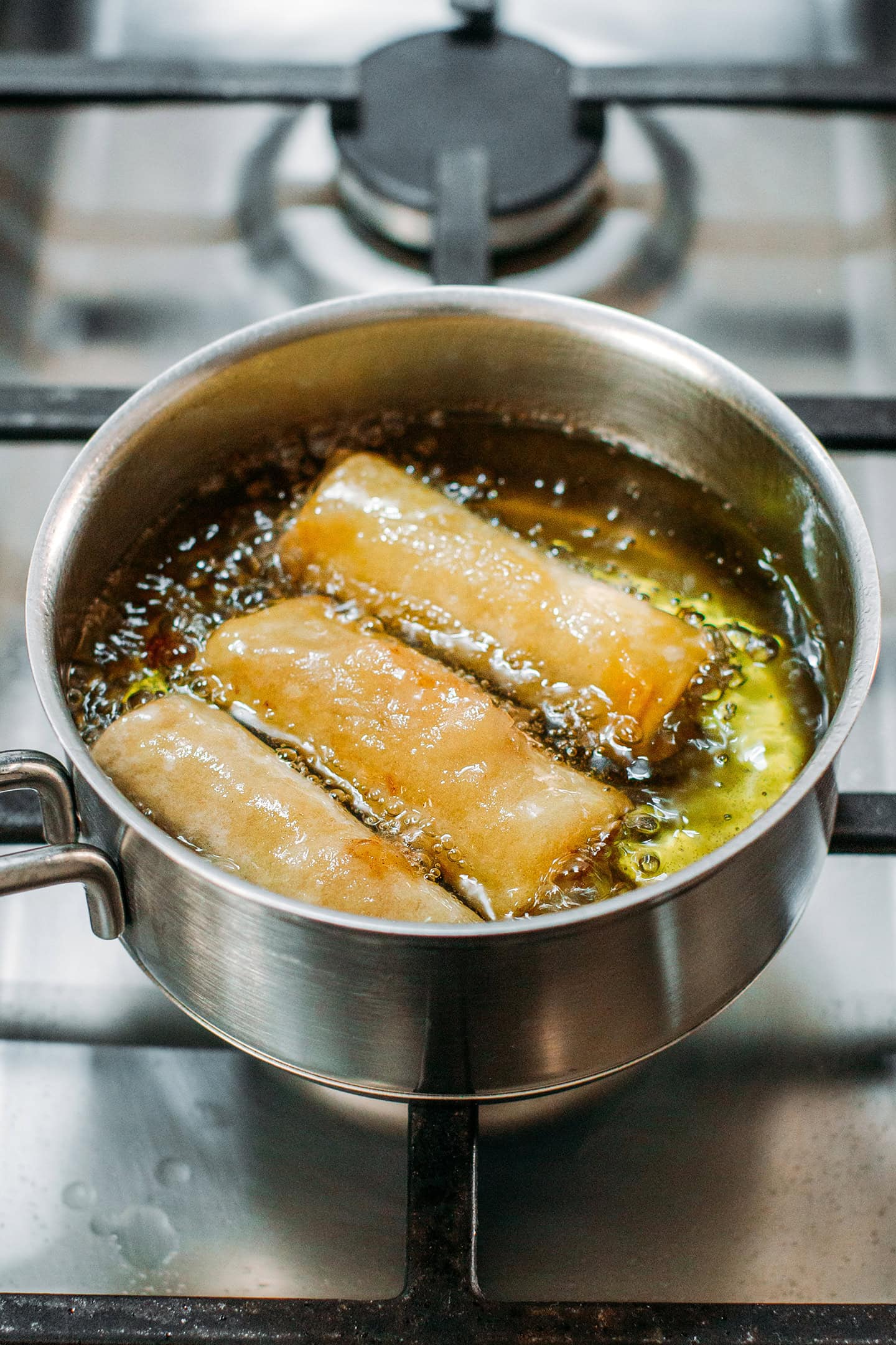 Apple egg rolls frying in a saucepan.