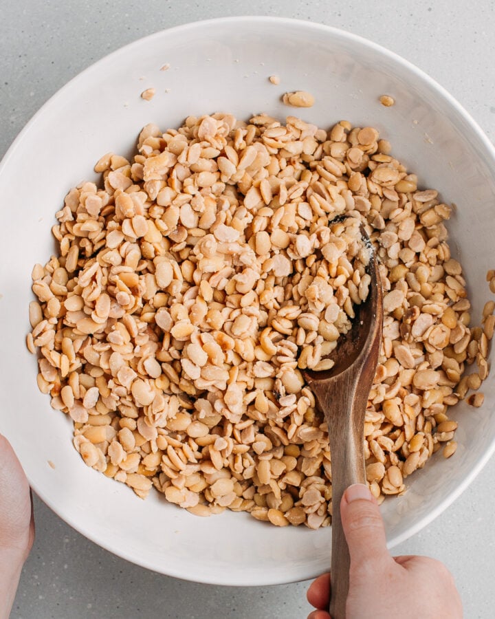 Tossing cooked soybeans with tempeh starter in a bowl.