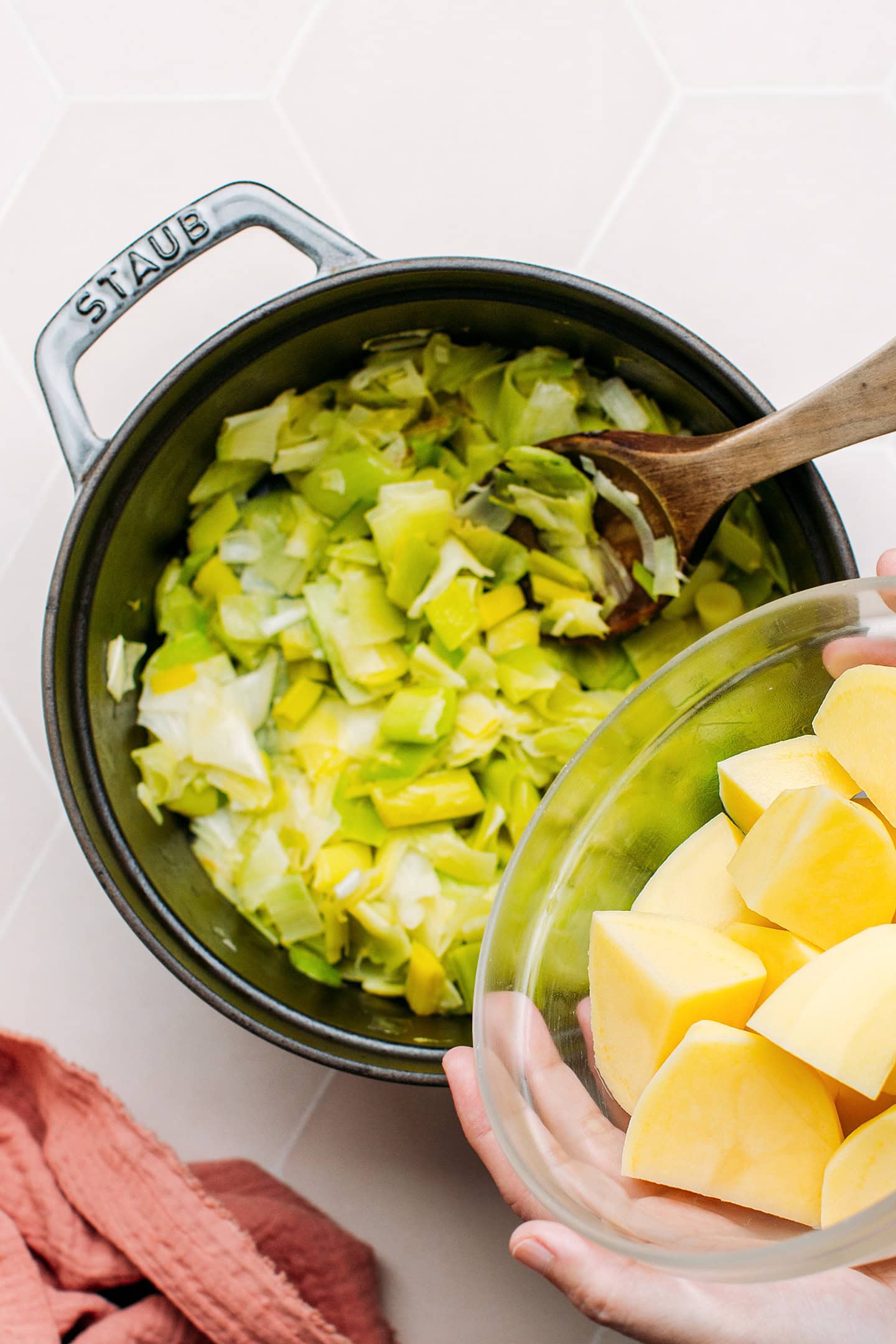 Adding diced potatoes to a pot containing sautéed leeks.