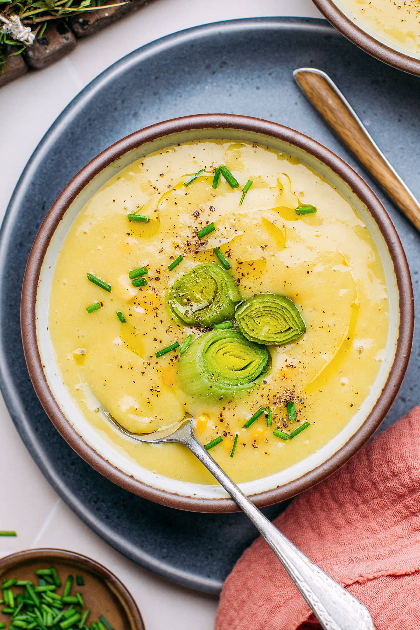 A bowl of potato leek soup topped with sautéed leeks, chives, and ground black pepper.