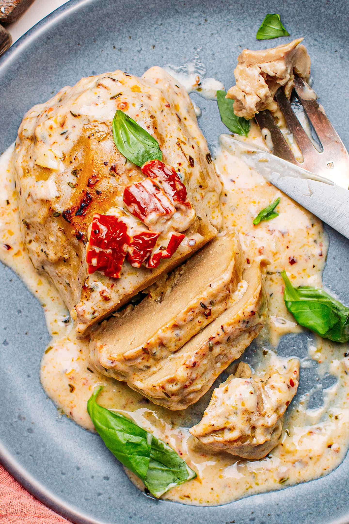 Close-up of vegan chicken breast coated with a creamy sauce and topped with sun-dried tomatoes.